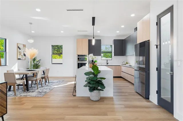 a kitchen with stainless steel appliances kitchen island granite countertop a refrigerator a stove a sink dishwasher and a dining table with wooden floor