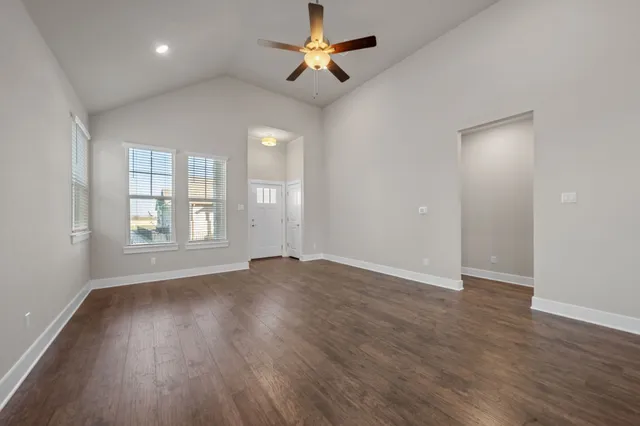 an empty room with wooden floor chandelier fan and windows
