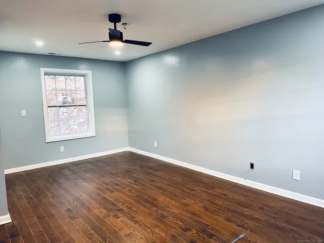an empty room with wooden floor chandelier fan and windows