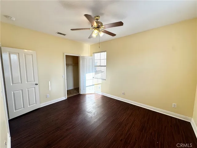 a view of an empty room with wooden floor and a ceiling fan