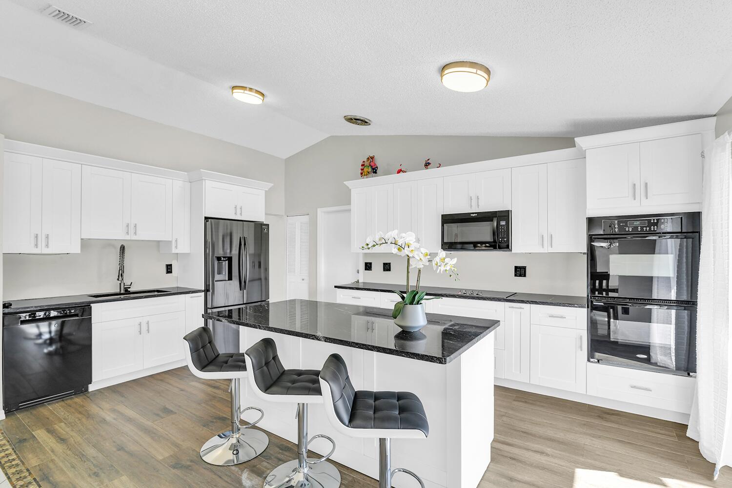 6335 Hitchin Post Way Delray Beach, FL 33484 - Photo 3 of 33 a kitchen with stainless steel appliances granite countertop a sink a stove a refrigerator cabinets and a dining table with wooden floor