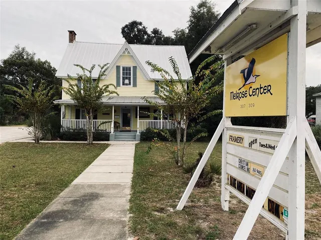 a view of a white house with a yard plants and large tree