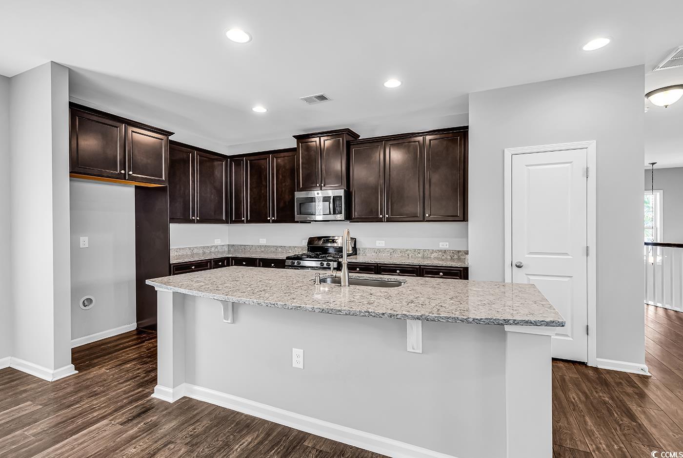 161 Splendor Circle Murrells Inlet, SC 29576 - Photo 8 of 37 Kitchen with dark brown cabinetry, light stone countertops, recessed lighting, dark wood-type flooring, and stainless steel microwave