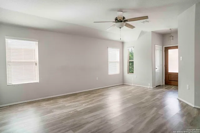 an empty room with wooden floor chandelier fan and windows