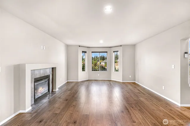a view of an empty room with wooden floor fireplace and a window