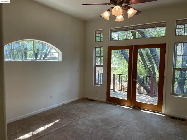 an empty room with a chandelier fan and windows