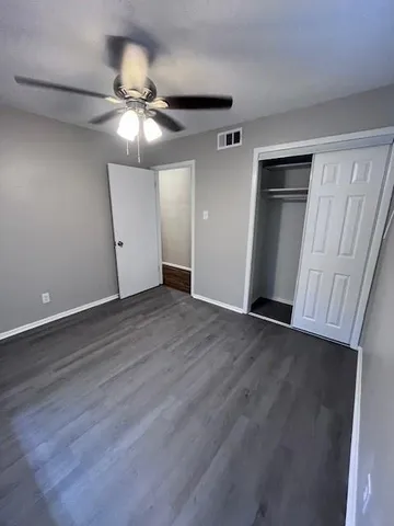 a view of an empty room with wooden floor and a ceiling fan