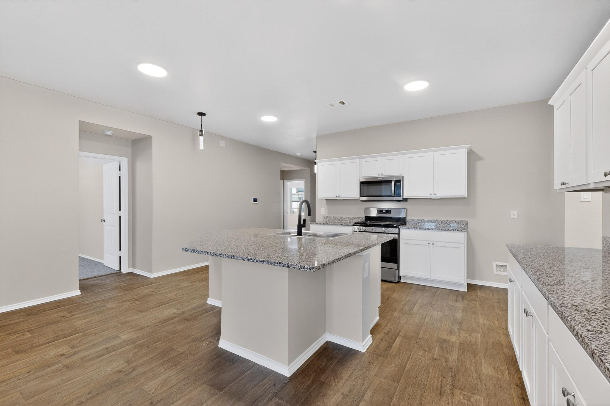 218 Sickle Loop Kyle, TX 78640 - Photo 9 of 34 Kitchen featuring stainless steel appliances, decorative light fixtures, a center island with sink, light stone counters, and light wood-style floors