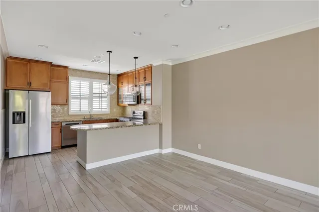 a kitchen with granite countertop a refrigerator a sink dishwasher a stove and white cabinets with wooden floor