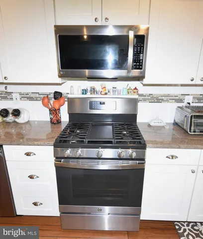 a large kitchen with sink a microwave oven a stove and a dining table with wooden floor