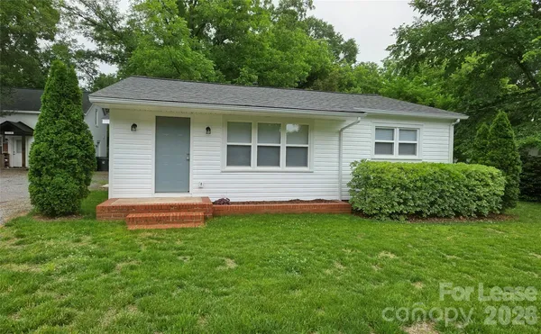 a view of a house with a yard plants and large tree