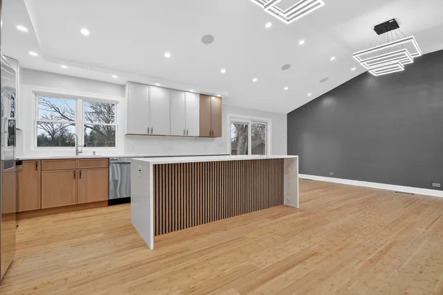 a large kitchen with stainless steel appliances granite countertop a large counter top a wooden floors and a large window