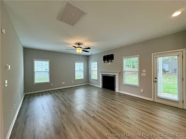 an empty room with wooden floor fireplace and windows