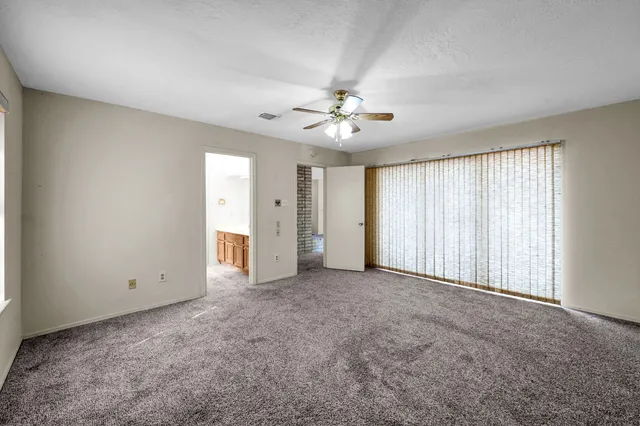 an empty room with chandelier fan and windows