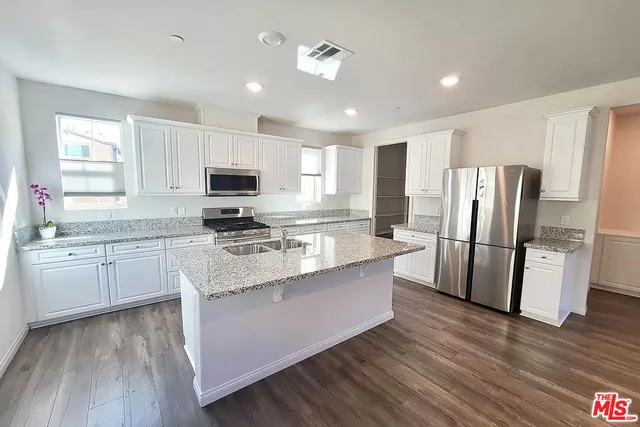 a kitchen with granite countertop a refrigerator a sink dishwasher a stove and white cabinets with wooden floor