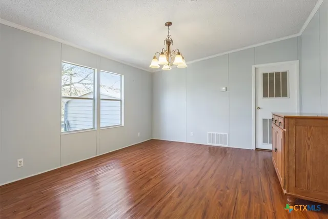 an empty room with wooden floor chandelier and windows