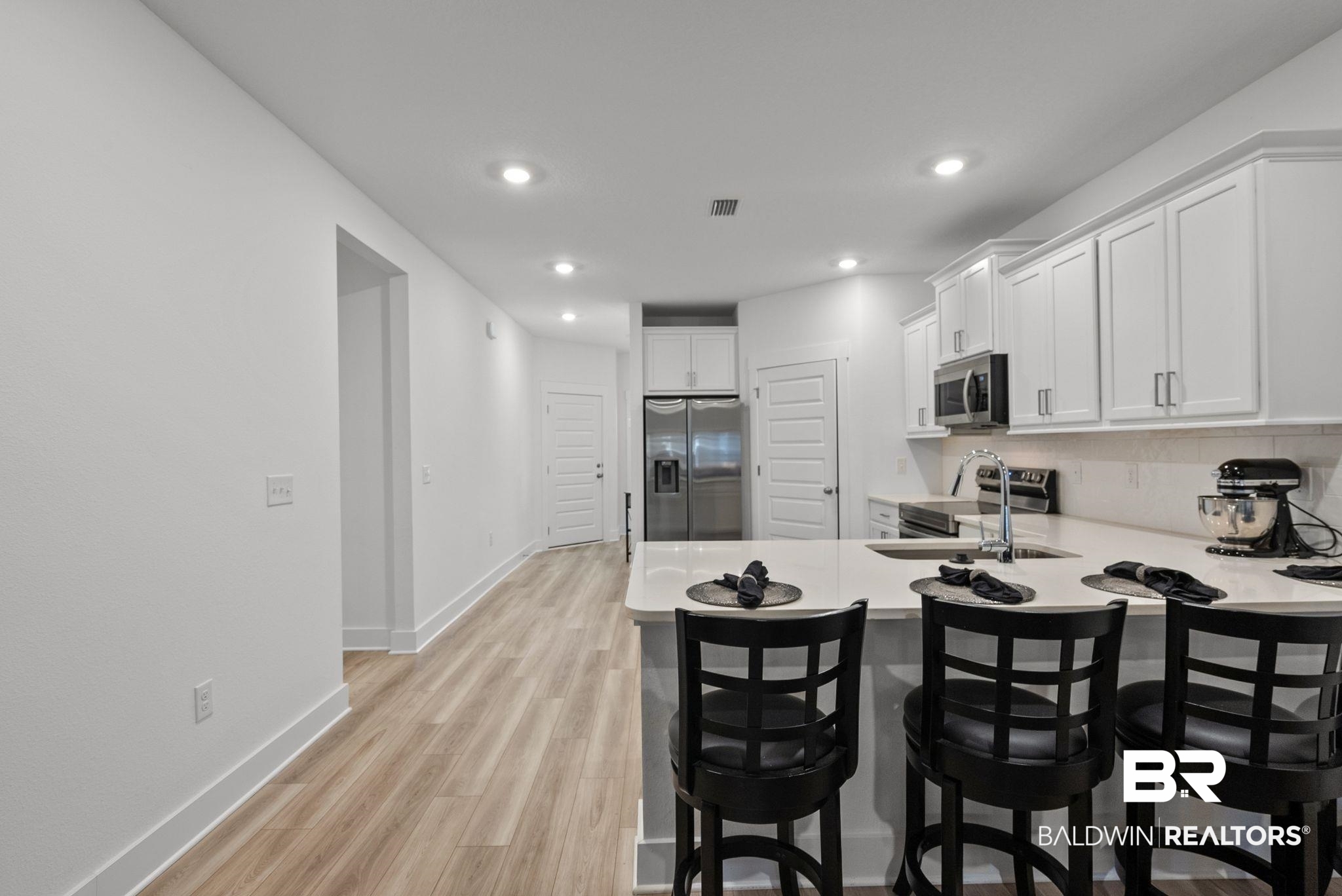 9899 Willet Way Foley, AL 36535 - Photo 10 of 37 Modern kitchen featuring an island with a breakfast bar, white cabinetry, stainless steel appliances, a white tile backsplash, and light wood-finish flooring throughout