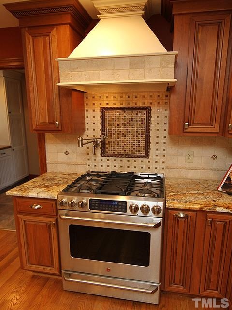 8036 Hawkshead Road Wake Forest, NC 27587 - Photo 11 of 25 Closer view of the Gas Range, magnificent granite, a chef's pot-fill faucet, detailed tile backsplash, and custom hood millwork and trim.