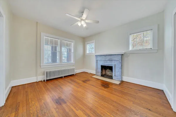 a view of an empty room with wooden floor fireplace and a window