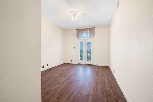 an empty room with wooden floor chandelier fan and windows