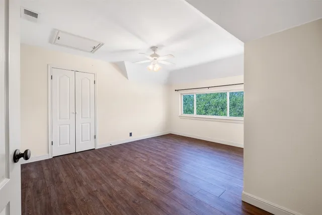 an empty room with wooden floor chandelier fan and windows