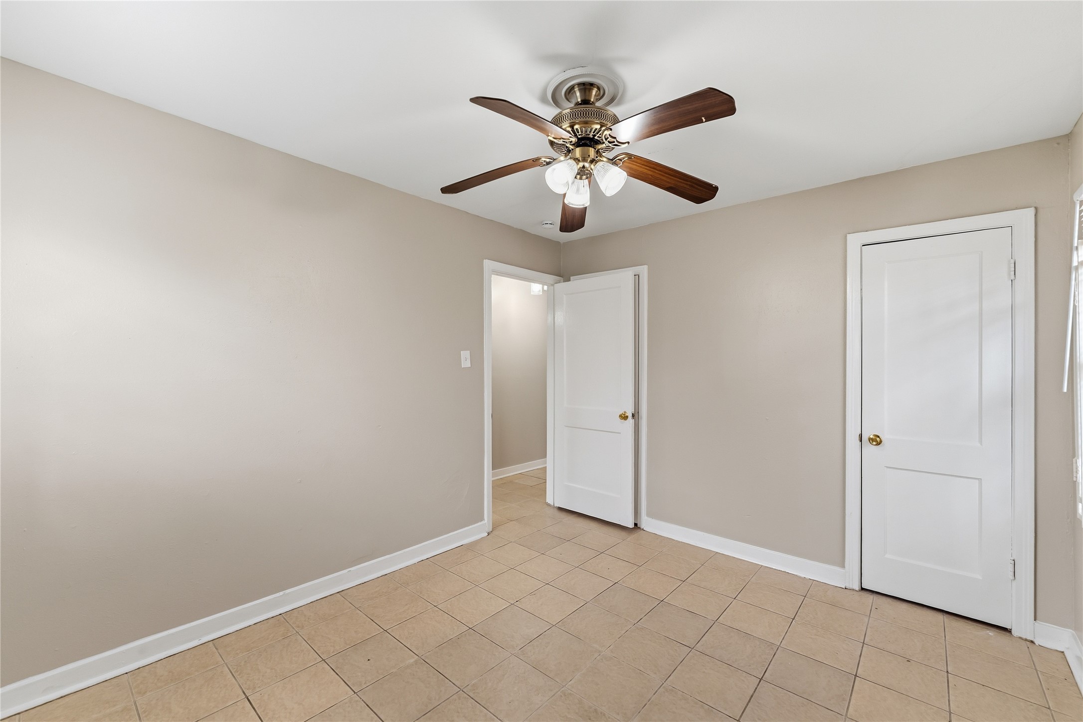 4814 Burma Road Houston, TX 77033 - Photo 11 of 16 This room features neutral walls, tiled flooring, and a ceiling fan with lights. It has two doors and a window, offering a spacious and versatile area suitable for various uses.