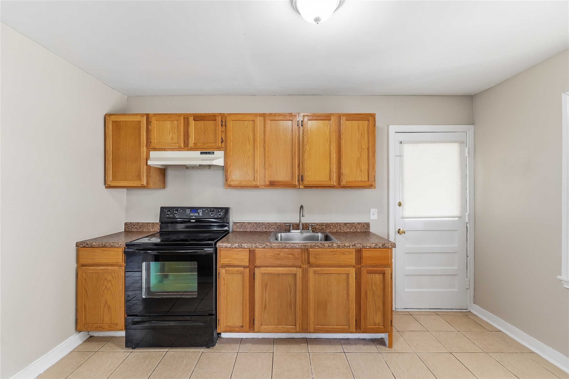 4814 Burma Road Houston, TX 77033 - Photo 4 of 16 Kitchen features wooden cabinets, a black stove, and a double sink. It has tiled flooring and a back door, creating a functional and simple space.