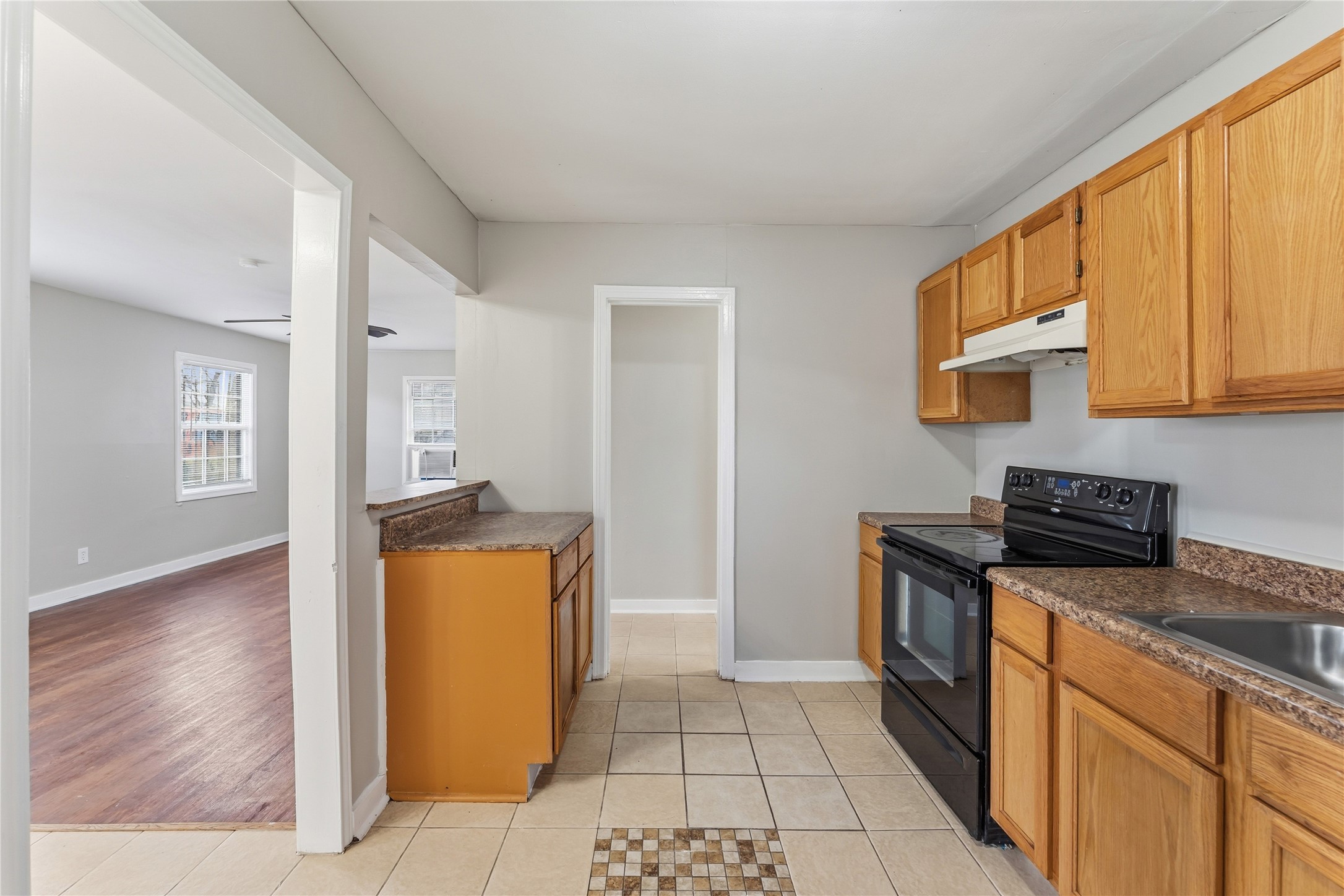 4814 Burma Road Houston, TX 77033 - Photo 6 of 16 Kitchen with wood cabinets, granite countertops, and an electric stove. It features tiled flooring and opens to a bright living area with hardwood floors and large windows.