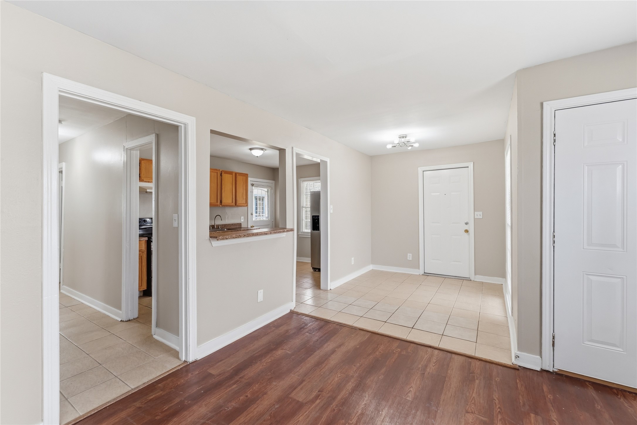 4814 Burma Road Houston, TX 77033 - Photo 7 of 16 Open entryway with a mix of tile and wood flooring. It features neutral walls, a small kitchen pass-through with natural wood cabinets, and multiple doorways leading to other rooms.