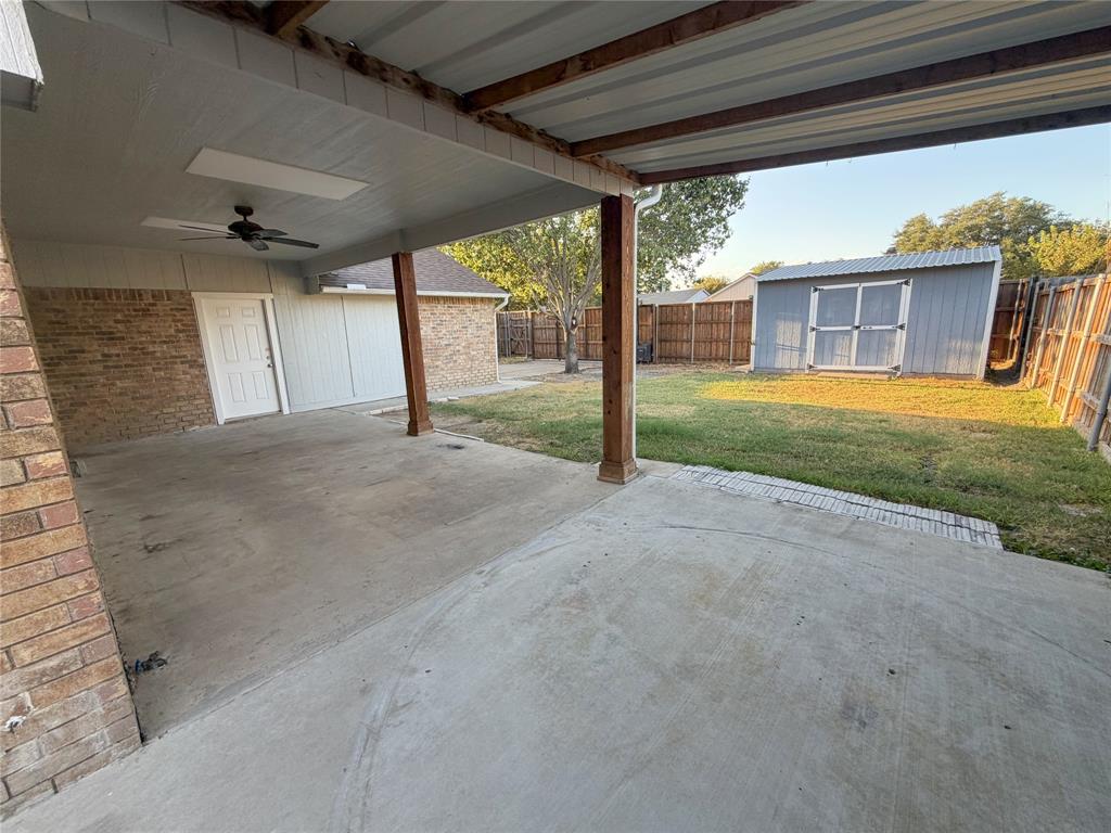 8601 Woodside Road Rowlett, TX 75088 - Photo 13 of 22 Covered concrete patio with ceiling fan, brick exterior, wood fence, and storage shed
