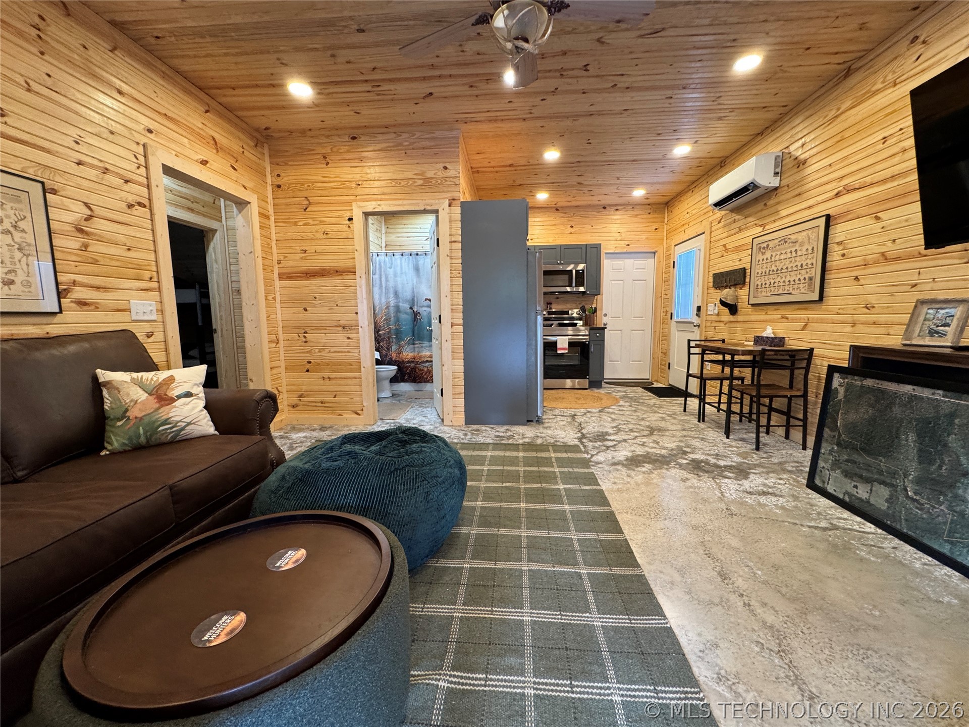 20862 East 1160th Road Keota, OK 74941 - Photo 19 of 47 Open-concept living space with wood-paneled walls and ceiling, recessed lighting, and a kitchen area featuring dark cabinetry, stainless steel appliances, and a compact dining set