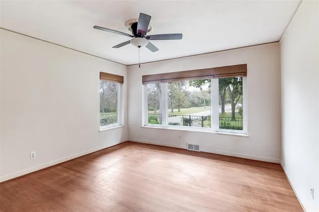 an empty room with wooden floor fan and windows