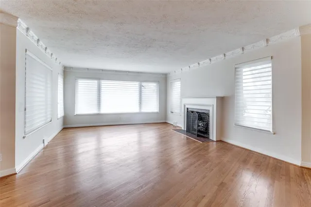 an empty room with wooden floor fireplace and windows