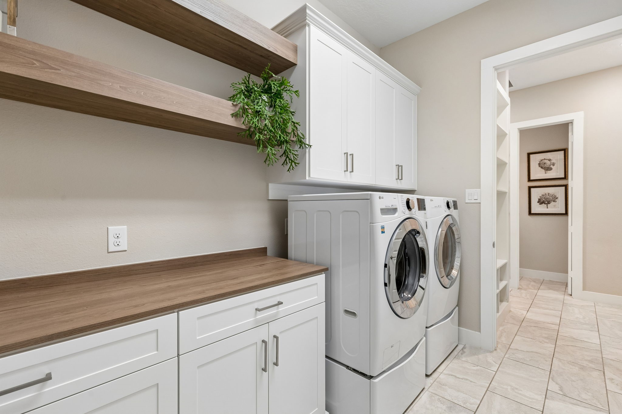 6514 Woodleaf Lake Loop Katy, TX 77493 - Photo 20 of 32 This laundry room is a masterclass in organization, featuring custom floating wood shelves and sleek white cabinetry with modern hardware. The space offers abundant counter space for folding and is finished with premium tile flooring that carries through from the main living areas.