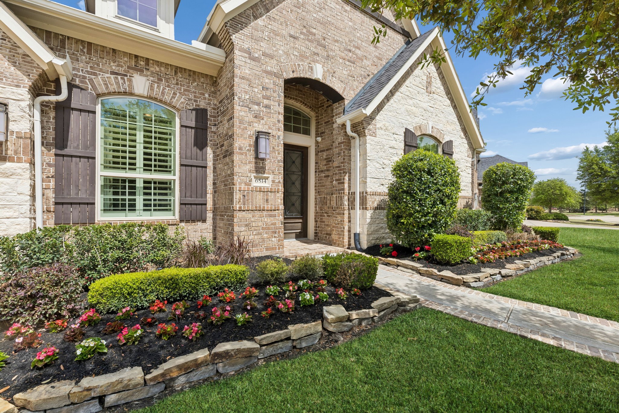 6514 Woodleaf Lake Loop Katy, TX 77493 - Photo 29 of 32 This close-up of the front entrance highlights the home's exceptional curb appeal, featuring a meticulously manicured lawn and vibrant, professional landscaping framed by natural stone edging.