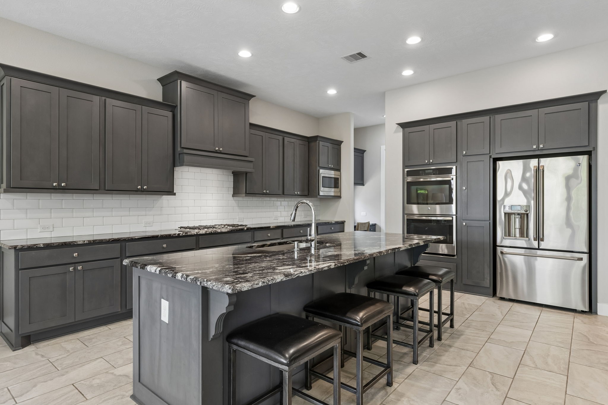6514 Woodleaf Lake Loop Katy, TX 77493 - Photo 3 of 32 The chef’s kitchen features an oversized granite island with a breakfast bar and sleek, dark-toned custom cabinetry. Professional-grade appliances include a premium gas cooktop, double convection ovens, and a high-end refrigerator.