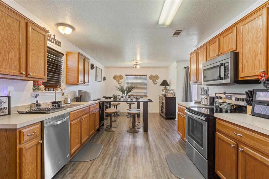 10817 Lilry Road Waco, TX 76708 - Photo 11 of 27 Kitchen with stainless steel appliances, light countertops, dark wood-type flooring, a textured ceiling, and wood finish cabinetry