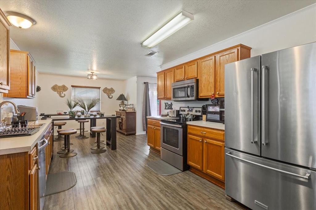 10817 Lilry Road Waco, TX 76708 - Photo 12 of 27 Kitchen with stainless steel appliances, light countertops, a textured ceiling, dark wood-style flooring, and wood finish cabinetry