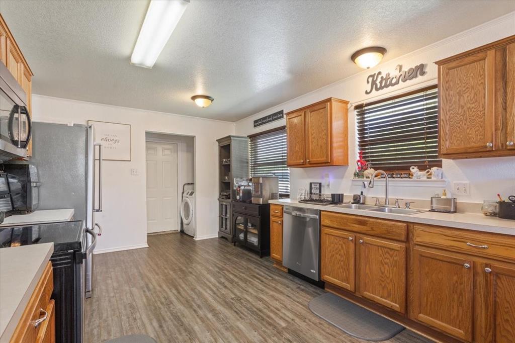 10817 Lilry Road Waco, TX 76708 - Photo 14 of 27 Kitchen with a textured ceiling, light countertops, wood finish cabinets, stainless steel appliances, and dark wood finished floors