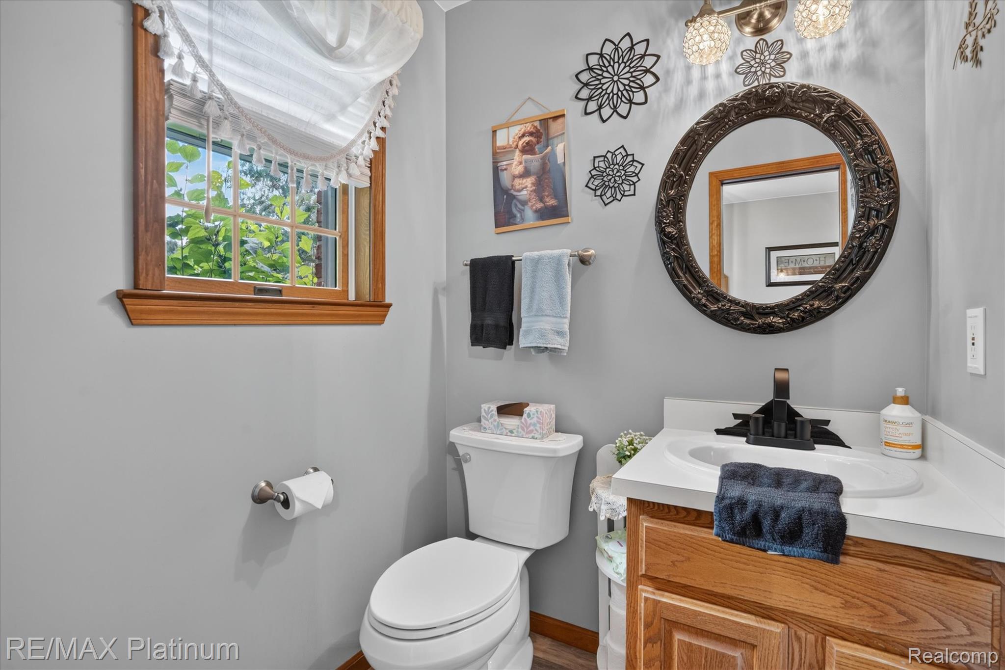 4457 Bradley Road Gregory, MI 48137 - Photo 27 of 79 Bathroom featuring a wood-framed window, a vanity with a white countertop and a built-in sink, a dark-framed round mirror, and a wall-mounted light fixture with three sconces