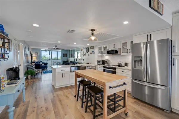 a kitchen with stainless steel appliances kitchen island granite countertop a stove top oven a sink dishwasher a refrigerator and a dining table with wooden floor