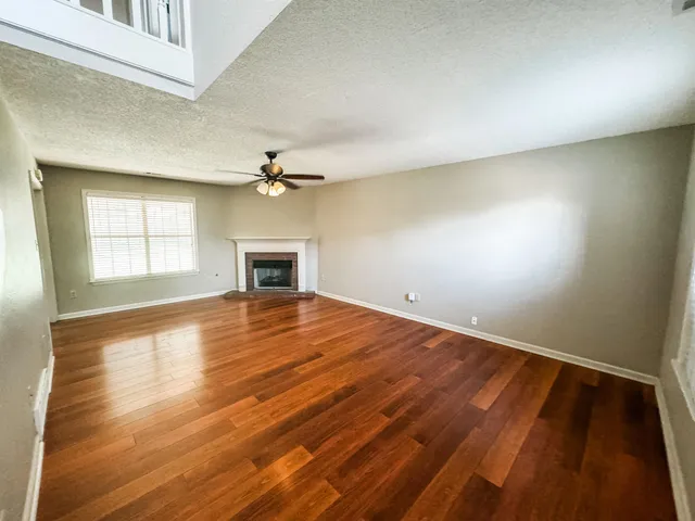 an empty room with wooden floor fireplace and windows