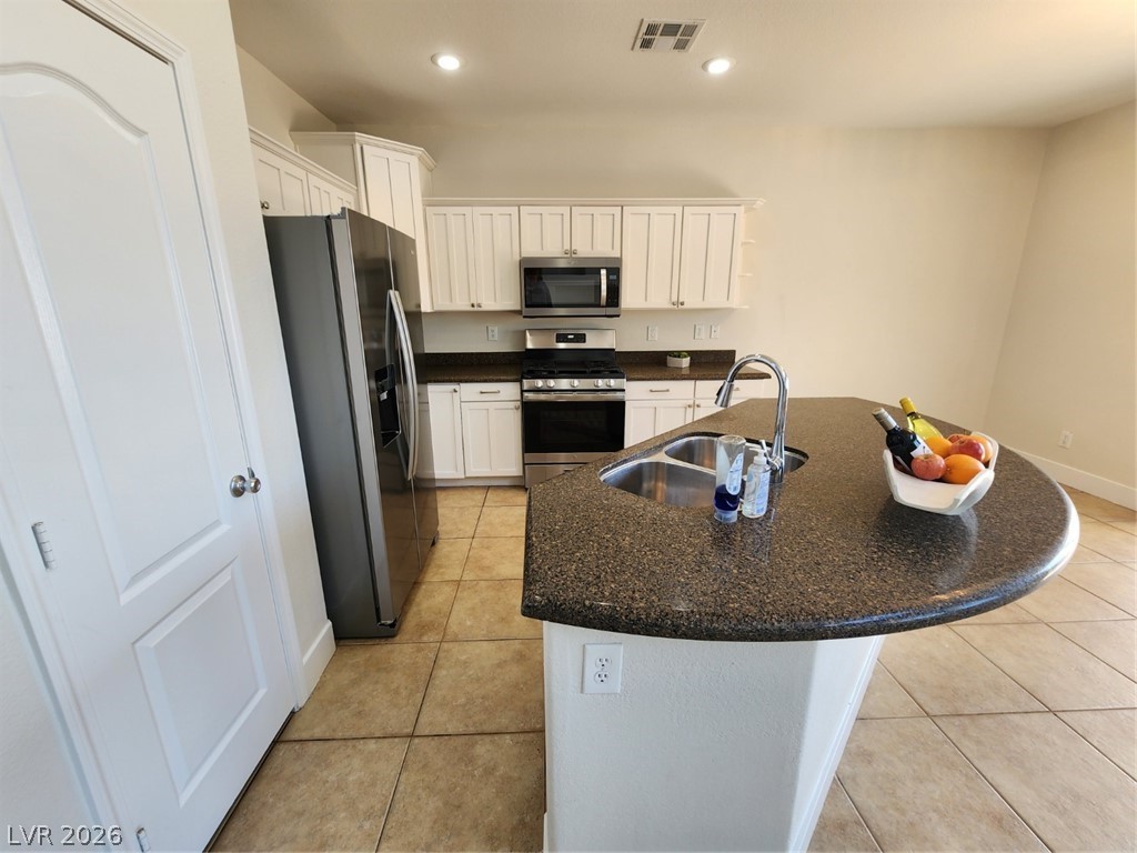 716 Sharon Hills Street Henderson, NV 89052 - Photo 11 of 66 Kitchen with fridge, stainless steel gas range, white cabinets, dark stone counters, and a kitchen island with sink