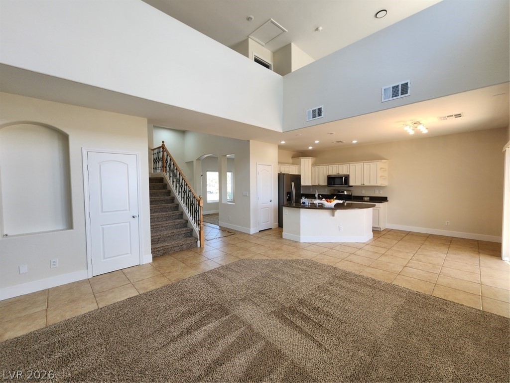 716 Sharon Hills Street Henderson, NV 89052 - Photo 8 of 66 Unfurnished living room featuring light tile patterned floors, arched walkways, light colored carpet, recessed lighting, and a high ceiling