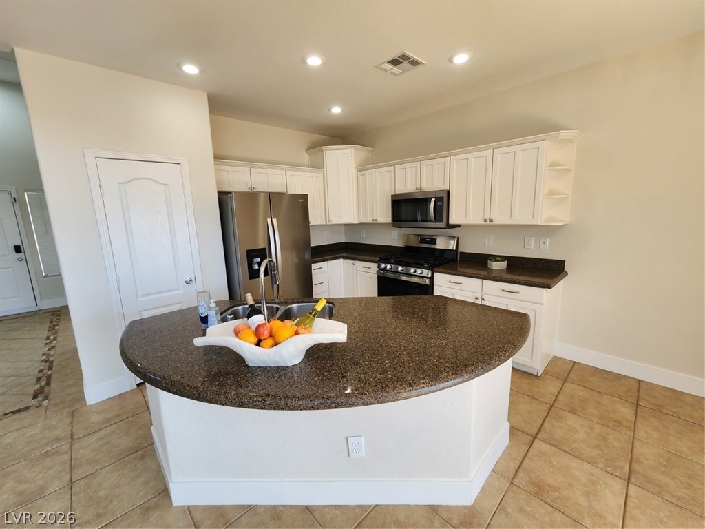 716 Sharon Hills Street Henderson, NV 89052 - Photo 9 of 66 Kitchen with stainless steel appliances, white cabinetry, dark stone counters, open shelves, and an island with sink
