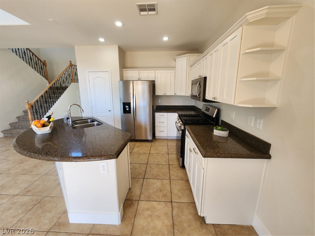 716 Sharon Hills Street Henderson, NV 89052 - Photo 10 of 66 Kitchen featuring open shelves, stainless steel appliances, a kitchen island with sink, dark stone counters, and white cabinets