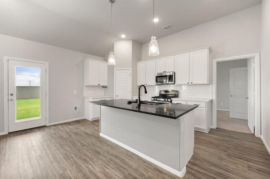 6910 Prairieside Trail Venus, TX 76084 - Photo 13 of 40 The kitchen features white cabinetry, stainless steel appliances, a black island countertop, and pendant lighting