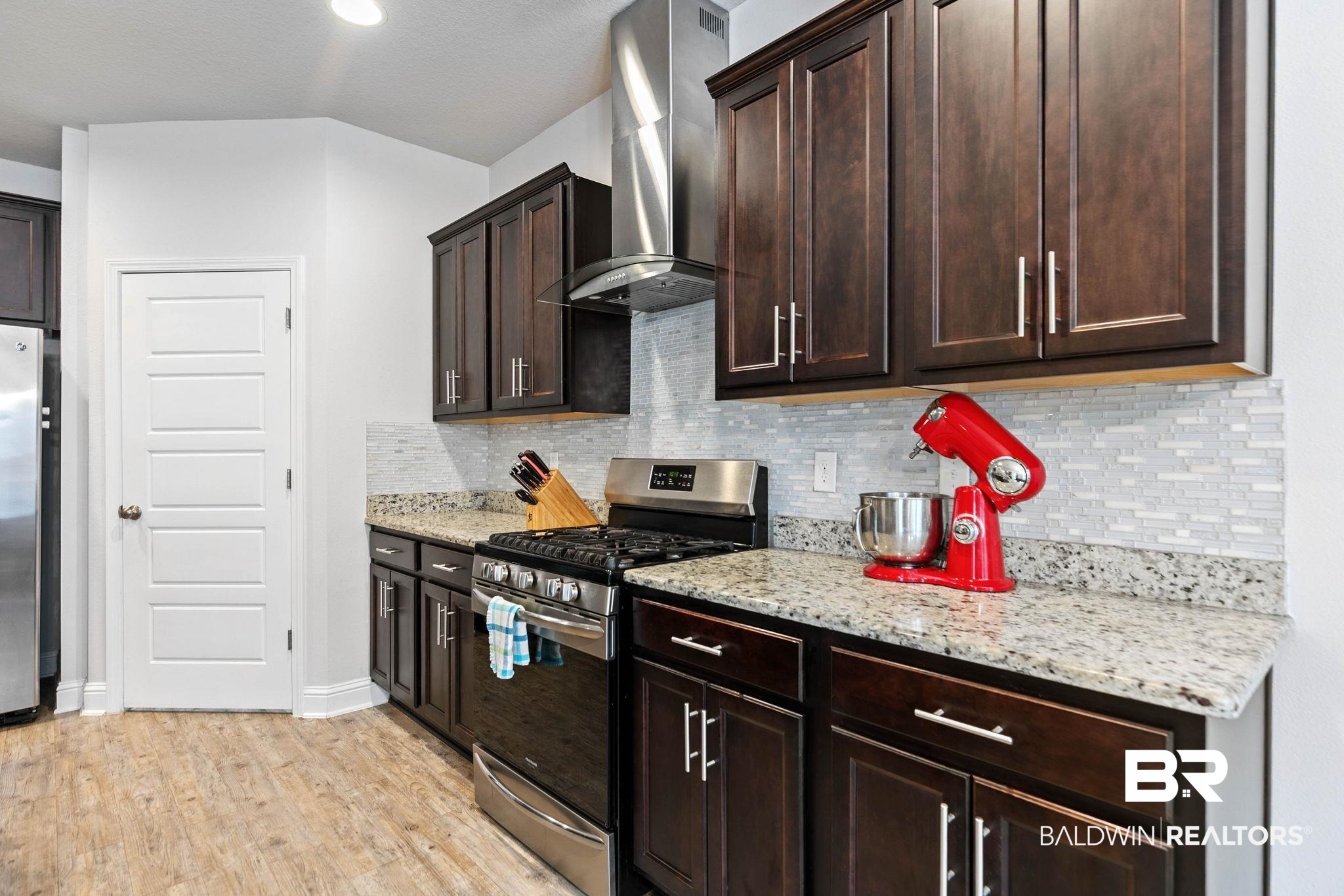 31350 Hoot Owl Road Daphne, AL 36527 - Photo 18 of 94 Kitchen featuring stainless steel appliances, dark wood finish cabinets, light stone countertops, light wood-style flooring, and tasteful backsplash