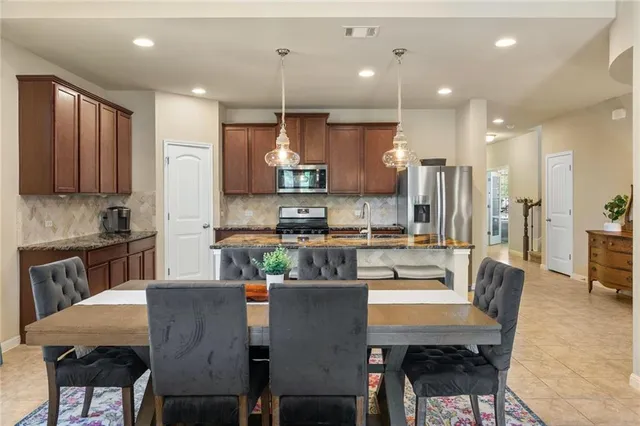 a kitchen with stainless steel appliances kitchen island granite countertop a dining table chairs refrigerator and sink