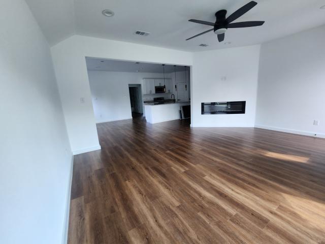 562 Jonelle Avenue Dallas, TX 75217 - Photo 11 of 20 Unfurnished living room with dark wood-type flooring, a ceiling fan, vaulted ceiling, and a glass covered fireplace